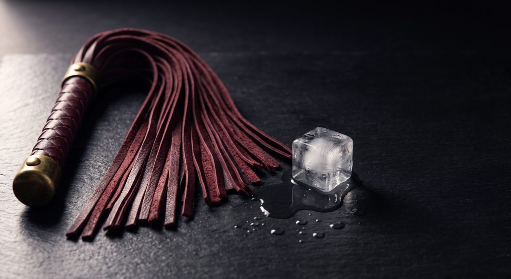 rôle de sadique BDSM, martinet de cuir et glaçon sur ardoise sombre