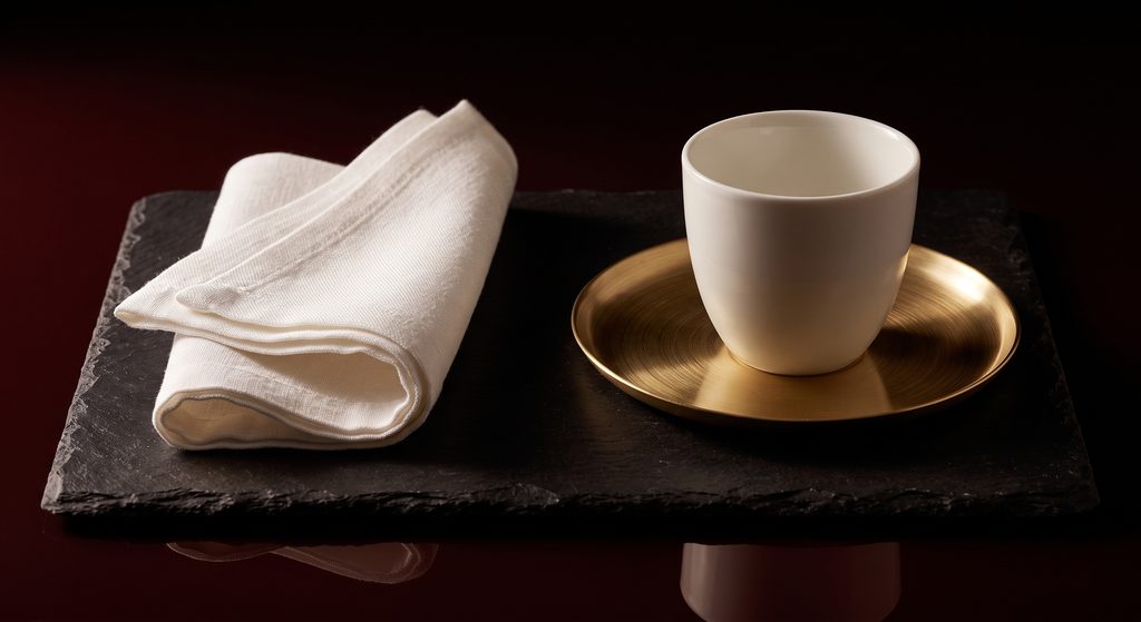 soumission de service, linge plié, plateau de laiton et tasse sur ardoise sombre